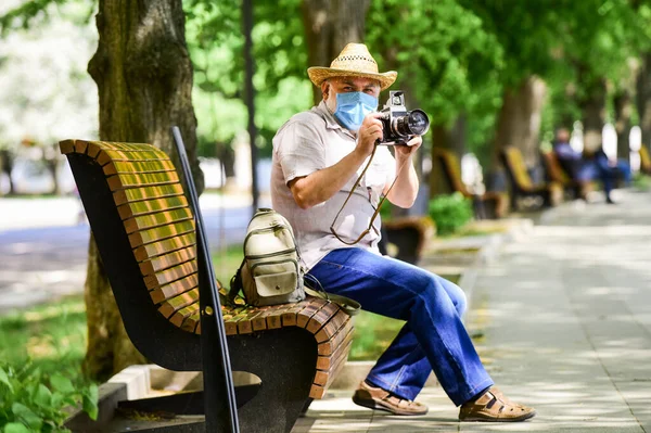 Élvezd a szépséget. a betegségtől való félelem. fényképész kamerával a padon. nyilvános helyek látogatásának tilalma. Idősebb férfi orvosi maszkban. Öreg ember pihenjen a parkban. élet a coronavirus lezárása alatt — Stock Fotó