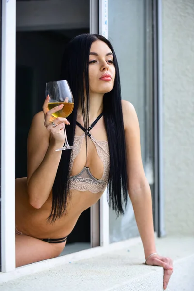 Házibuli. Elit bor. Sokat tud az élvezetekről. Hedonizmus koncepció. Dögös nő erotikus fehérneműben ül az ablakpárkányon. A nő bort iszik. Szexi lány alkoholos koktéllal. Szexi lány egy pohár borral — Stock Fotó