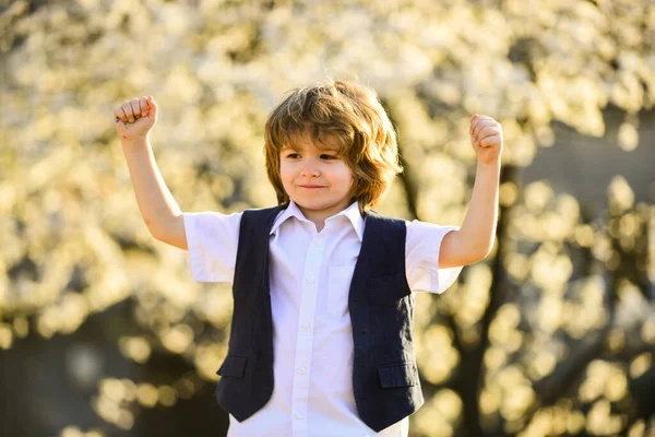 俺の勝ちだ。子供の頃の幸せ。屈託のない少年が外を歩く。春の木を咲かせている男の子。幸せな子供は健康な髪をしている。夏と春のファッション。子供は花の自然を部分的に楽しむ — ストック写真