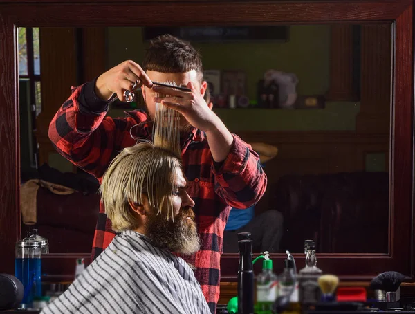 Haare spenden. Scharfer Gegenstand in Gesichtsnähe und Spritzen lenkt den Halter ab. Spenden- und Charity-Konzept. Kerl mit gefärbten blonden Haaren. Haare schneiden. Friseursalon. Hipster bekommen Haarschnitt — Stockfoto