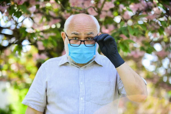Slim en beschermd. gezond leven. dragen masker in bloeiende roze sakura park. Een man met een beschermend masker. Bloeiende bloemen ruiken op coronavirus quarantaine. voorzorgsmaatregelen te nemen tijdens de pandemie — Stockfoto