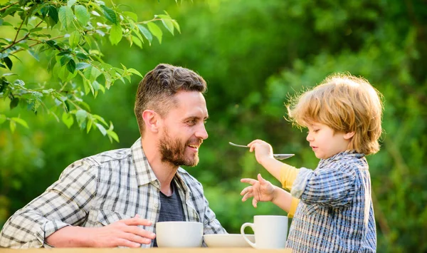 Dad and boy eat and feed each other outdoors. Ways to develop healthy eating habits. Feed your baby. Natural nutrition concept. Feeding son natural foods. Stage of development. Feed son solids — Stock Photo, Image
