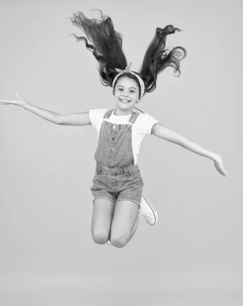 Liten flicka hoppa gul bakgrund. Full av energi. En aktiv flicka känner frihet. Roligt och avslappnande. känna sig fri. bekymmersfri unge på sommarlovet. Dags för skoj. retroskönhet i luften. Hopp av lycka — Stockfoto