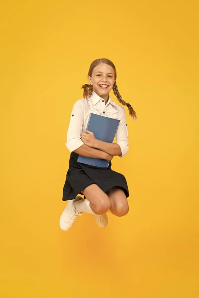 De volta ao conceito de escola. Menina de fundo amarelo. A rapariga da escola gosta de estudar. Aluno emocional. Entusiasmado por estudar. Criança feliz pulando em uniforme escolar. A divertir-me. Saltar e sentir-se livre — Fotografia de Stock