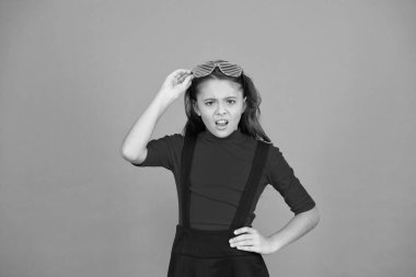 Gözlüklü, turuncu arka planda bir kız. Etkinlik ve eğlence. Parti kutlaması. Parti aksesuarı. Eğleniyorum. Karnaval partisi. Maskeli balo konsepti. Çocuk gözlük takıyor. Göz giyimi mağazası.