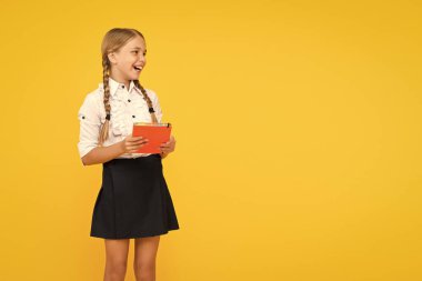 İyi bilginin neşesi. Sarı arka plan üzerine kitap tutan sevimli küçük bir kız. Kitaptan bilgi alan sevimli küçük okul çocuğu. Bilgi ve beceriler. Bilgi günü veya 1 Eylül, boşluğu kopyala