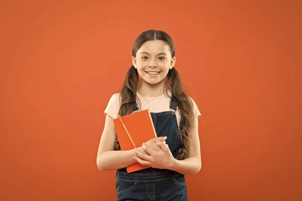 Livre préféré. heureuse petite fille avec cahier. livre de lecture. leçon de littérature. retour à l'école. écolière sur fond orange. journal intime pour enfants. écrire des notes. poésie et roman. éducation moderne — Photo