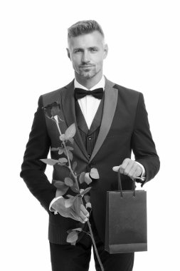 Erkek zarafeti. Sevgililer günü siyah smokin takımı. Aşk randevusu için hediyeli bir adam. Resmi etkinlikler için siyah kravat. Gül ve alışveriş çantalı smokin giyen adam. Sevgililer günün kutlu olsun. Sevgiyle hediye. Alışveriş satışı