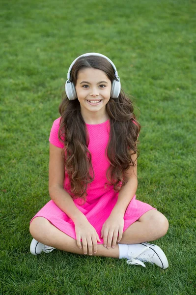 教育用ポッドキャスト。子供の女の子は音楽の緑の草の牧草地を楽しむ。楽しい時間だ。私の夏のプレイリスト。屋外でリラックスしながら音楽を聴く。子供のヘッドフォンは音楽を聞く。女の子のヘッドフォン｜リスニングミュージック — ストック写真