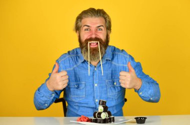 Asya yemeği. Suşi siparişi. Adam evde suşi yiyor. Çubuklu suşi ve zencefil. Japon mutfağı. Doğu kültürü. Sakallı hippi rulo yiyor. Japon yemek teslimatı. Suşi rulo