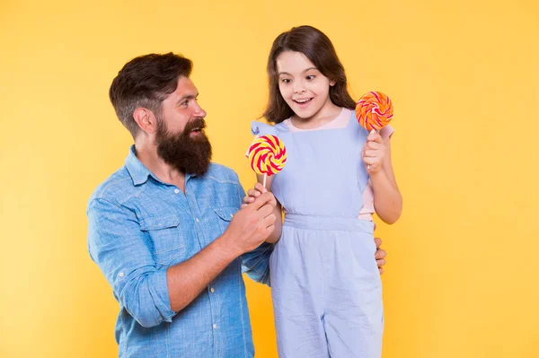Taste the rainbow. Family of father and daughter eat candies. Happy family yellow background. Bearded man entertain little child with treats. Family time. Love and trust. Fun thing family do together