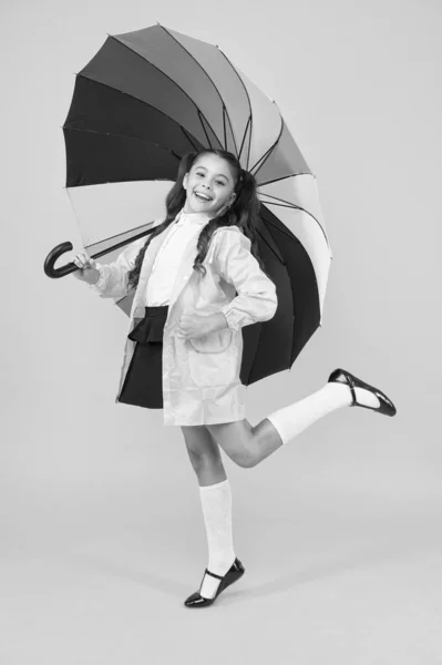 아이들을 위한 가을 패션. 어린 소녀는 우산 밑에서 편안 함을 느낀다. 화려 한 우산을 두른 행복 한아이. 트렌디 레인 코트입은 쾌활 한 여학생. 가을 비가 오는 날씨에 대비 한다 — 스톡 사진