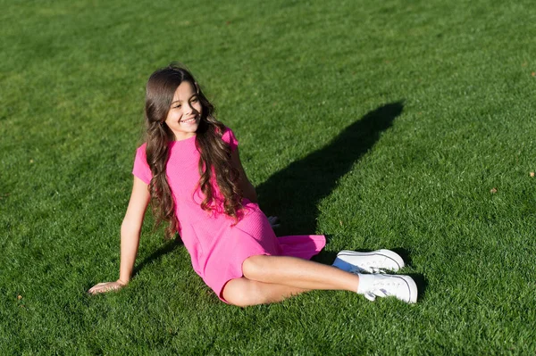 O que faz a criança feliz. Férias. Ideias de férias. Menina sorridente feliz desfrutar relaxar no gramado. Aluna alegre. Diverte-te. Menina bonito garoto sentar grama verde. Criança feliz emocional relaxando ao ar livre — Fotografia de Stock