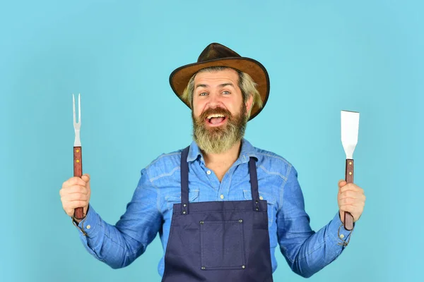 Farmer reklámozza a nagy horderejű felszerelést. Steaket főzök. Főzőeszközök. Nyári piknik. Bbq amerikai hagyomány. Kulináris fogalom. Félig átsütve. BBC kaja. A szerszámok húst sütnek. Férfi kötényben tartsa barbecue grill — Stock Fotó