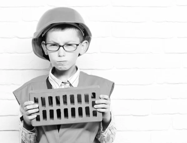 Young cute builder boy on white brick wall background, copy space — Stock Photo, Image