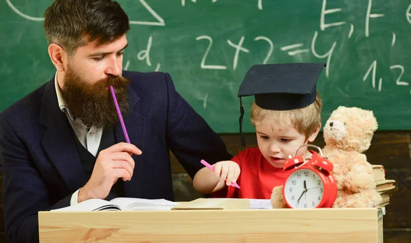 教室ではモーターボードの正式な着用と生徒の先生,背景に黒板.ホームタスクをチェックする父は少年を助ける、息子。先生と一緒に勉強する熱狂的な子供。ホタスクの概念 — ストック写真