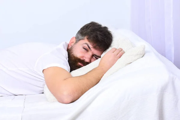 Homem de camisa deitado na cama, parede branca no fundo. Conceito de sesta e sesta. Macho com barba e bigode dormindo, relaxando, dormindo, descansando. Cara no rosto cansado dormindo em lençóis brancos e travesseiro . — Fotografia de Stock