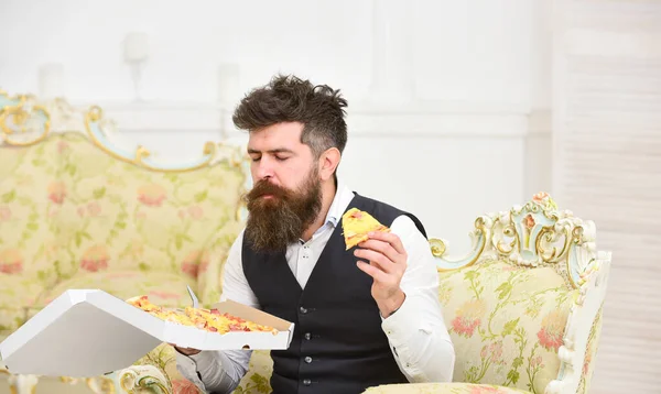 Macho dans les vêtements classiques faim, détient tranche de pizza au fromage, mange, profiter du goût, fond intérieur. Concept de livraison de pizza. Homme avec barbe et moustache tient boîte avec savoureuse pizza chaude fraîche — Photo