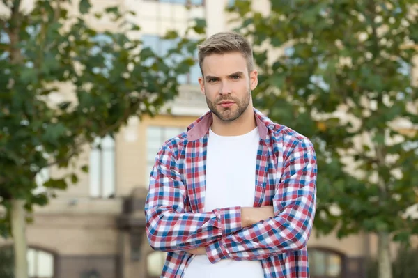 Hezký chlapík stojí venku se zkříženýma rukama. Charismatický módní model. Pohledný neoholený muž. Muž nosí kostkovanou košili. Mužská krása a móda. Jarní móda pro muže. Důvěrné umístění — Stock fotografie