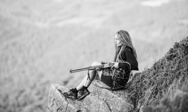 Av sezonu. Hunter Dağları manzara arka planı. Seksi bir savaşçı. Çekici, uzun saçlı, güzel yüzlü, av tüfeği tutan bir kadın. Nişan alma konsepti. Amazon kızı uçurumda oturur av için silah hazırlar.