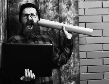 Kaba sakallı, beyaz tenli hippi elinde dizüstü bilgisayar ve el işi kâğıdı tutuyor.