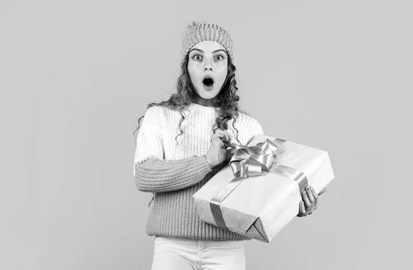 Ребенок держит коробку на желтом фоне. Рождественская распродажа подарков. Пусть ваше Рождество будет ярким. С зимними праздниками. удивлена маленькая девочка вязала шляпу и свитер. Счастливого Рождества! — стоковое фото