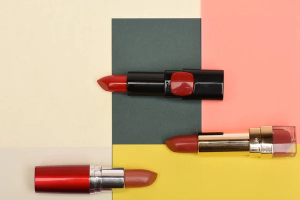 Tres lápices labiales rojos, escarlata yacían sobre fondo beige, rosa, amarillo , — Foto de Stock