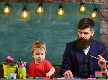 Aile meşgul yüzler yaratıyor, çiziyor. Öğretmen ve çocuk arka planda karatahtayla sınıfta. Baba ve oğul çalışma odasında birlikte resim yapıyorlar. Ders çizimi kavramı.