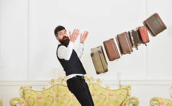 Poggyászbiztosítási koncepció. Porter, komornyik, óvatlan, régi bőröndöket dobál le. Férfi szakállal és bajusszal klasszikus öltöny szállít poggyász, luxus fehér belső háttér — Stock Fotó