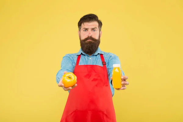 Свежий сок. Сжимающий смузи. Доставка свежих витаминов. Хипстерский коктейль. Человек бородатый шеф-повар держит органические натуральные помидоры и бутылку желтого фона. Вегетарианское питание. Смузи — стоковое фото
