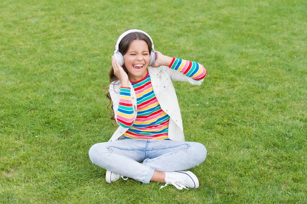Pleasant time. Child headphones listen music. Do not bother me. Cool girl headphones listening music. Educational podcast. Listen music while relaxing outdoor. Kid girl enjoy music green grass meadow