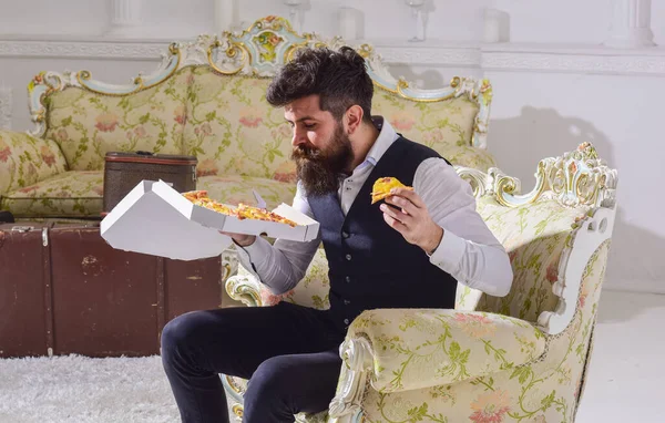 Mężczyzna z brodą i wąsami trzyma pudełko z pyszną pizzą. Koncepcja apetytu. Macho w klasycznych ubraniach głodny, posiada plasterek pizzy z serem, je, ciesząc się smakiem, tło wnętrza. — Zdjęcie stockowe
