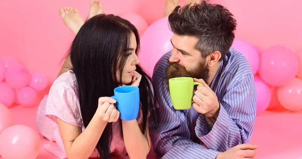 Pareja relajarse en la mañana con café. Concepto de fin de semana. Hombre y mujer con ropa de hogar, pijama. Hombre y mujer en rostros sonrientes yacían, fondo rosa. Pareja en amor beber café en la cama . — Foto de Stock