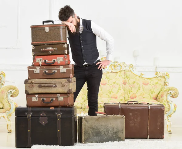 Gepäck- und Umzugskonzept. Macho elegant auf müdem Gesicht, erschöpft am Ende des Packens, stützt sich auf einen Stapel alter Koffer. Mann mit Bart und Schnurrbart gepackt Gepäck, weißer Innenraum Hintergrund. — Stockfoto