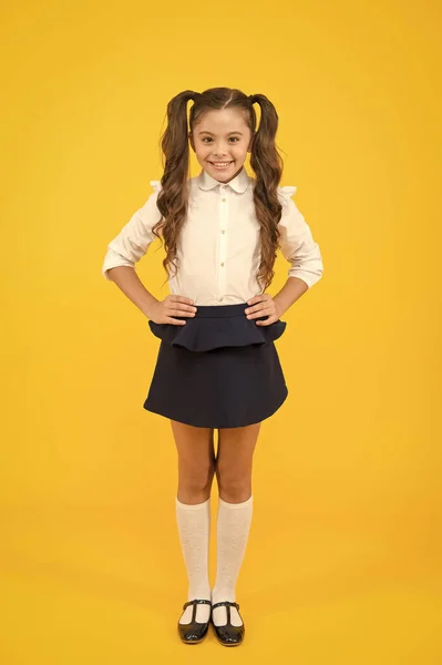 学校に戻るためのファッショントレンド。ファッションが黄色の背景に見える幸せな小学生。ファッションの制服で微笑む長い髪の小さな女の子。小さな学生のためのファッション — ストック写真