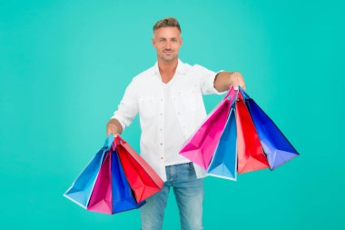 Alışveriş yap ve keyfine bak. Mutlu alışveriş yapan mavi arka plan. Yakışıklı adam alışveriş torbalarını tutuyor. Hediyelik eşya dükkanı. Tatil hazırlığı. Hediyelik eşya dükkanı. İndirim ve indirim. Düşene kadar alışveriş yap.