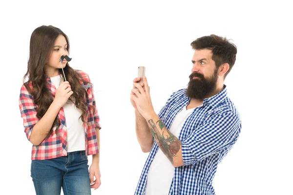 A fazer memórias de família. Homem barbudo tira uma foto de uma criança. Menina pequena posar com adereços bigode. Hipster usar telefone celular. Celebração familiar. Sessão de fotos de família. A família é tudo — Fotografia de Stock