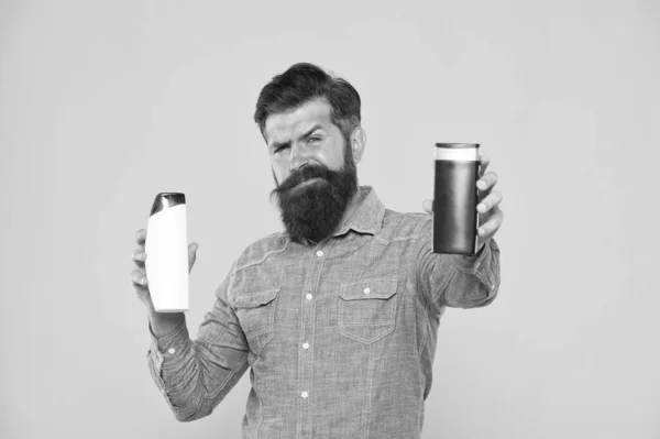 Toma este champô. Homem barbudo segurar frascos de xampu fundo amarelo. Hipster com barba e bigode escolher shampoo cabelo. Shampoo que deixa o cabelo brilhante. Cuidado com os cabelos. Lavagem de cabelo e corpo — Fotografia de Stock