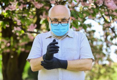Özellikle yaşlılar enfeksiyon kaptıysa risk altındalar. Yaşlandıkça bağışıklık sistemi enfeksiyonlarla mücadelede daha az etkili oluyor. Dışarıda maskeli ve eldivenli kıdemli bir adam var. Yaşlılara nasıl yardım edilir