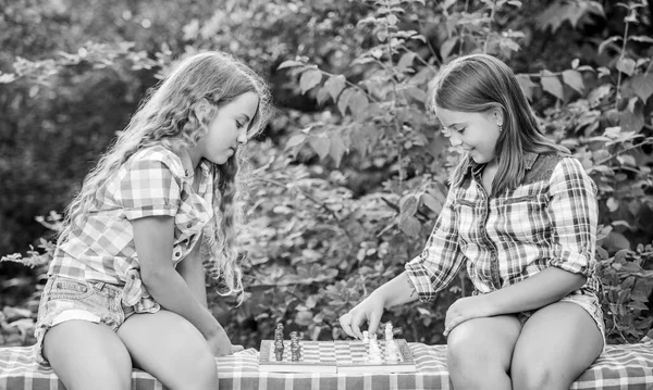 Sport and hobby concept. Little girls play chess. Sisters playing chess. Smart children. Early childhood development. Intellectual game. Think better. Children play chess outdoors nature background