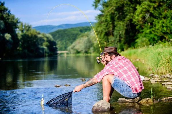 Pesca grande jogo. relaxar na natureza. pesca hipster com colher-isca. mosca peixe passatempo do homem. Hipster em camisa quadriculada. pescador bem sucedido na água do lago. maduro barbudo homem com peixe na haste — Fotografia de Stock