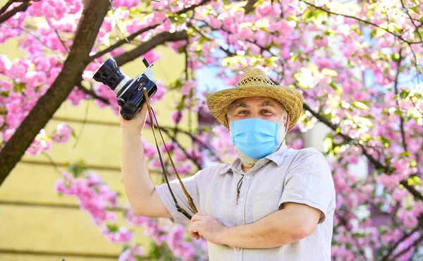 Férfi turista használja kamera fotózni cseresznyevirág. szakura a teljes virágos fotózás. Végzős szakállas férfi légzőmaszkban. professzionális fotós munka során koronavírus karantén. tavaszi férfi — Stock Fotó