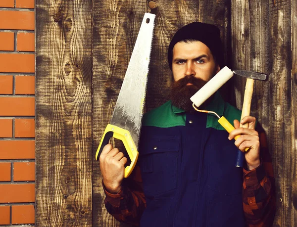 Pintor barbudo sosteniendo varias herramientas de construcción con cara seria — Foto de Stock