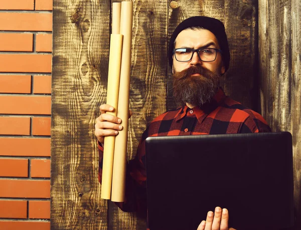 Bearded brutal caucasian hipster holding laptop and craft paper — Stock Photo, Image