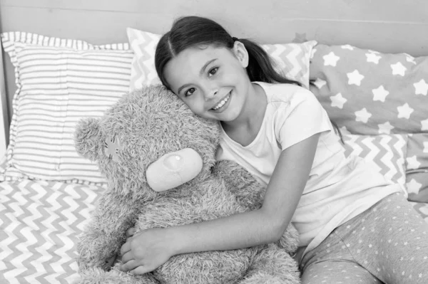 Rutinas nocturnas para niños. Juguete favorito. Niña abrazo osito de peluche en su dormitorio. Tiempo agradable en el acogedor dormitorio. Chica niño pelo largo lindo pijama relajarse y jugar peluche peluche oso juguete. Concepto de amor puro. — Foto de Stock