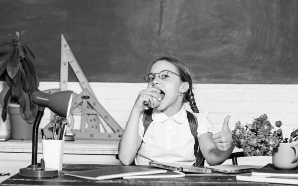 Μαθήτρια κάθεται γραφείο chalkboard φόντο. Μαθητής στο σχολείο. Κορίτσι μικρό παιδί τρώει μήλο σνακ. Σχολικές διακοπές. Χαλάρωσε ανάμεσα στα μαθήματα. Φόρτιση βιταμινών. Σχολική ζωή. Υγιής τρόπος ζωής — Φωτογραφία Αρχείου