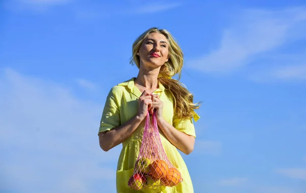 Vrouw met touwtje boodschappentas met fruit en brood op hemelse achtergrond. Geen afval concept. meisje in jurk met string bag shopper. tas met boodschappen. Herbruikbare eco tas om te winkelen — Stockfoto