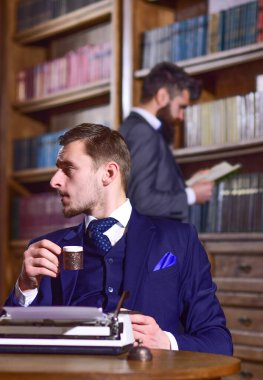 Kütüphanede arka planda antika kitapları olan takım elbiseli adamlar..