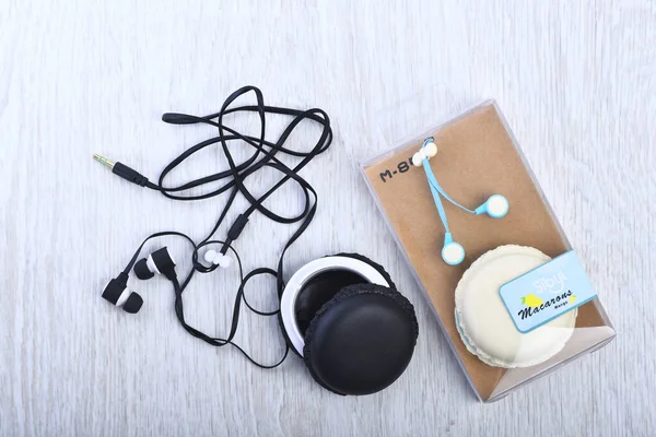 Earphones in black color near container on wooden background.