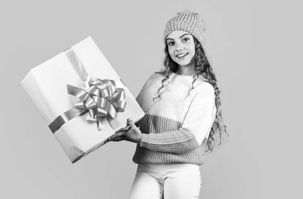 С Новым годом тебя. Счастливого Рождества вам. скидки на зимний отдых. Радостная маленькая девочка вязала шляпу и свитер. Ребенок держит коробку на желтом фоне. С Новым годом. Покупка подарков — стоковое фото